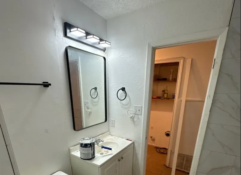 After: bathroom wall rebuild. Torn-out wall patched, textured and painted. New vanity light, mirror and hardware.