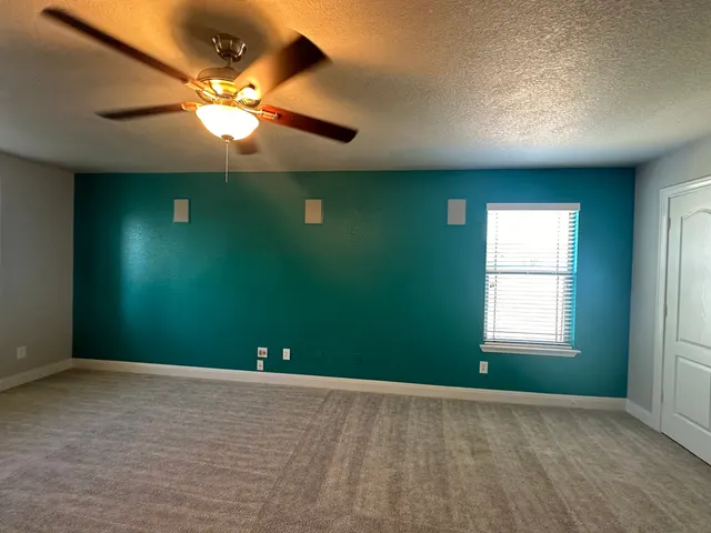 Bedroom with a teal accent wall, ceiling fan and new carpet