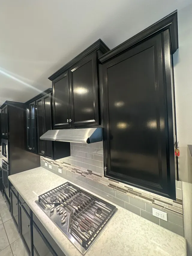 Kitchen upper cabinets painted glossy black above a gas cooktop