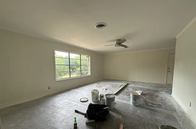 Living room mid-repaint with floors protected and paint buckets staged