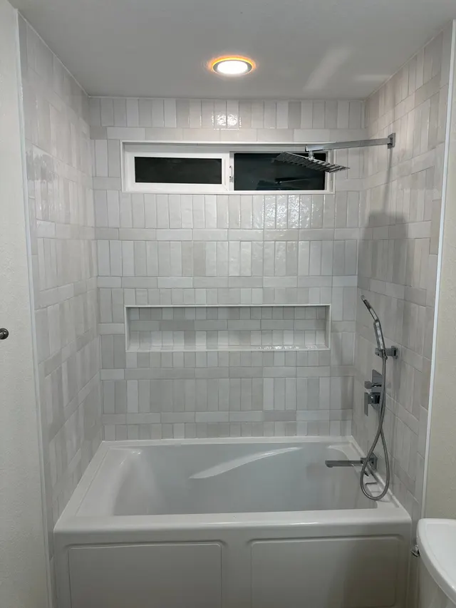 New white stacked-tile tub surround with a long niche and rain shower head